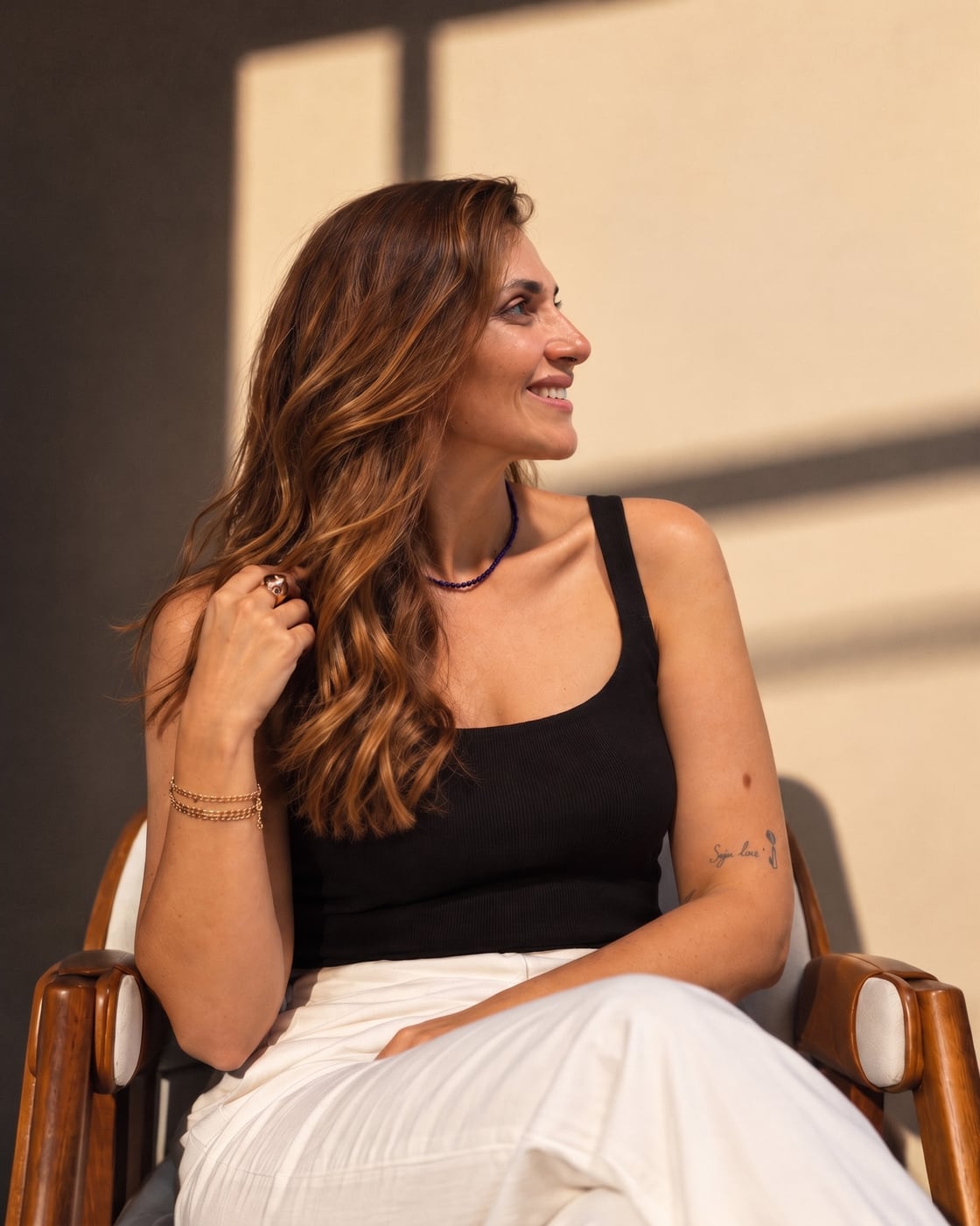 Malú Araújo sentada em uma cadeira de madeira, sorrindo, em um ambiente com luz natural